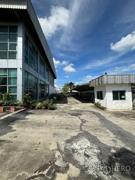 Warehouse for rent in Bang Phli, Samut Prakan - Side view of the warehouse with a security guardhouse and spacious concrete yard for truck access.