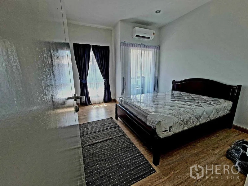 Detached House for rent or sale in Pathum Thani - Second bedroom with balcony-style glass doors, air conditioning and laminate floors.