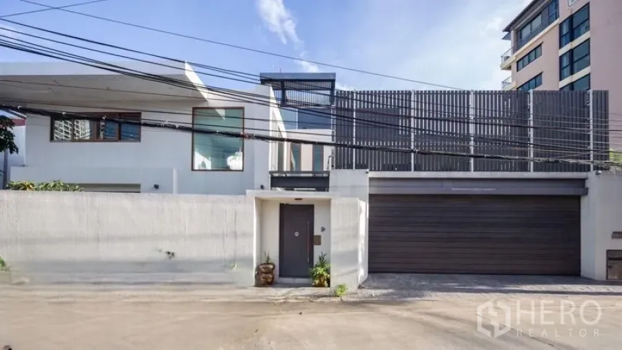 Detached House for sale in Chatuchak, Bangkok - Front elevation of gated modern house with wide garage door and vertical privacy screens.