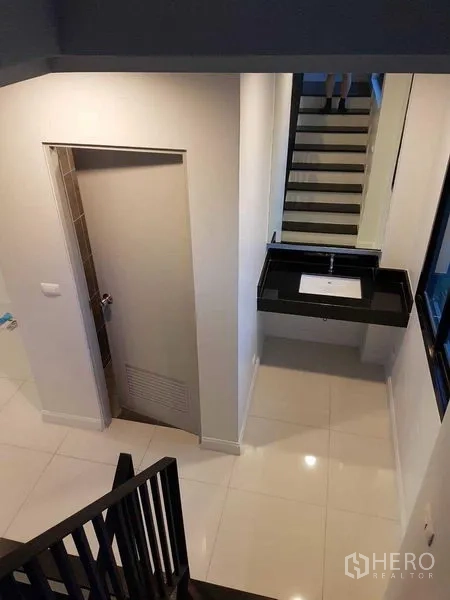 Shophouse for rent or sale in Bang Na, Bangkok - Stair landing view showing black staircase, sink and doorway.