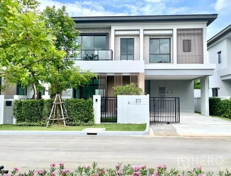 Detached House for rent or sale in Bang Phli, Samut Prakan - Front elevation of the modern house showing balcony, vertical slats, carport and trimmed hedges.