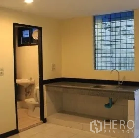 办公空间 出租在Bang Rak, Bangkok - 办公室茶水间，长台面与水槽，旁边为内部卫生间，灯光温暖。
