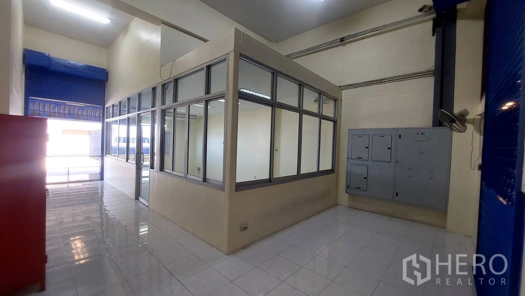 Warehouse for rent in Mueang Pathum Thani, Pathum Thani - Glass-walled supervisor office pod inside the warehouse near blue shutters.
