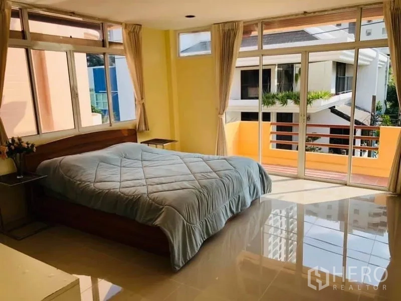 Detached House for rent in Watthana, Bangkok - Master bedroom with floor-to-ceiling glass doors opening to a balcony and glossy tile floors.