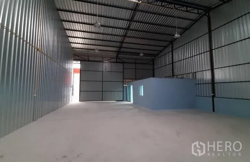 货栈 出租在Lam Luk Ka, Pathum Thani - 高挑仓库大厅，吊装照明，侧墙设有蓝色独立办公室。