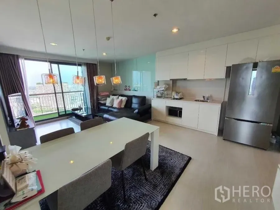 Condominium for sale in Khlong Toei, Bangkok - Open-plan living room and white kitchen with balcony access and floor-to-ceiling windows.
