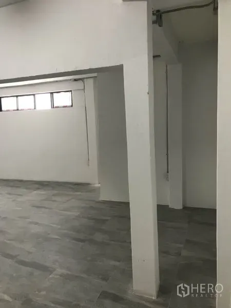 办公空间 出租在Watthana, Bangkok - 带结构立柱的办公分区，灰色地砖与上部狭长窗。