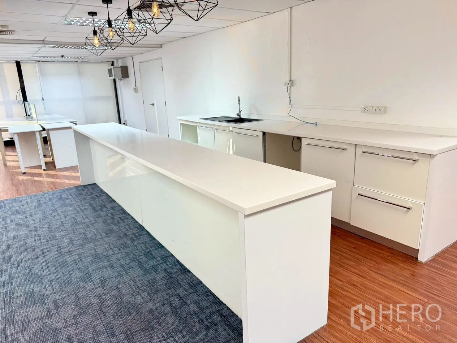 Office Space for rent in Watthana, Bangkok - Pantry area with a long white island, sink, storage cabinets, and pendant lights.
