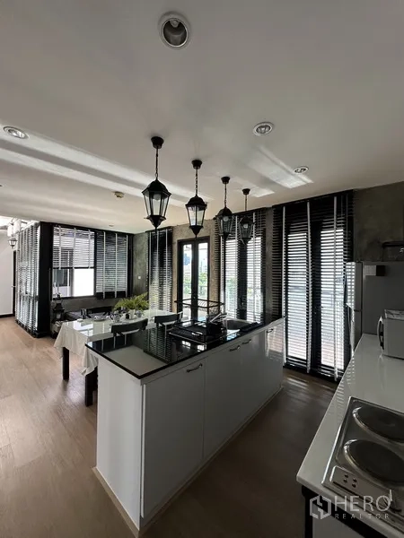 Condominium for rent in Khlong Toei, Bangkok - Sleek kitchen with central island cooktop, lantern pendants, and balcony access.