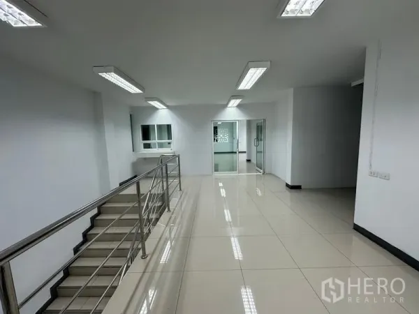 Warehouse for rent in Phra Nakhon Si Ayutthaya - Bright office corridor with tiled floors, fluorescent lights and stainless-steel stair rail.