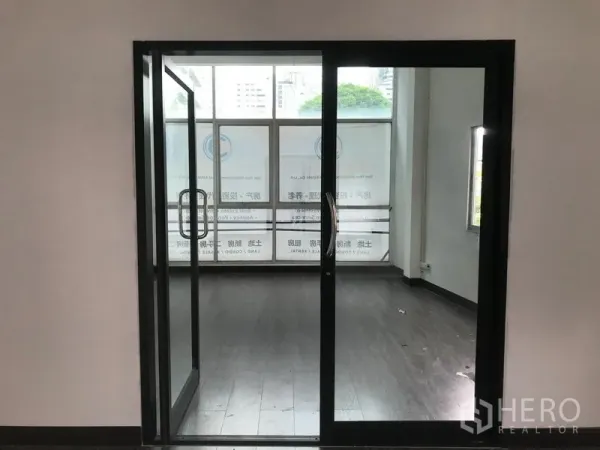 Shophouse for rent in Watthana, Bangkok - Black-framed sliding glass doors opening to a front room with large street-facing windows.