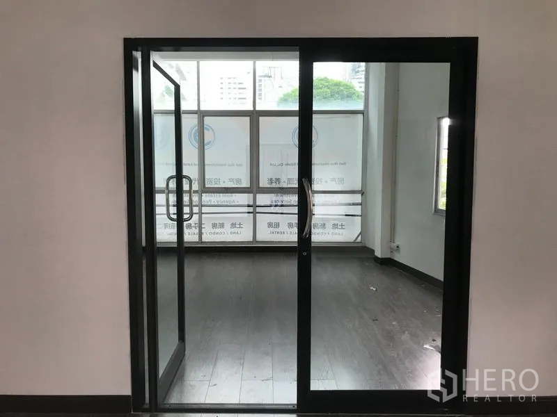 Shophouse for rent in Watthana, Bangkok - Black-framed sliding glass doors opening to a front room with large street-facing windows.