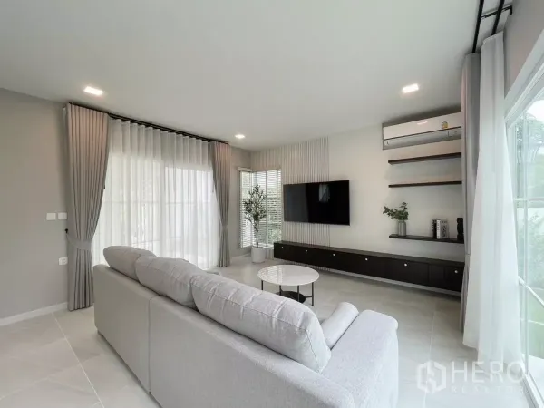 Detached House for rent in Bang Phli, Samut Prakan - Living area with built-in TV console, floating shelves, and corner windows with sheer curtains.