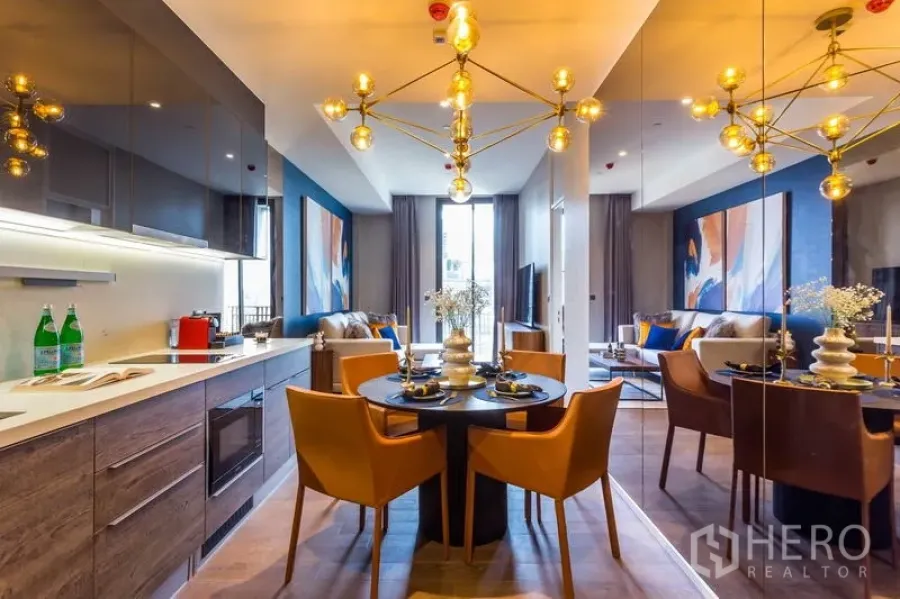 Condominium for rent or sale in Pathum Wan, Bangkok - Open-plan kitchen, dining and living area with gold chandelier, mirrored wall and balcony in a 1-bedroom condo in Pathum Wan, Bangkok.