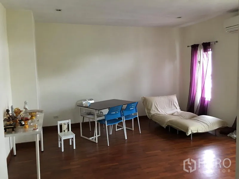 Townhouse for sale in Huai Khwang, Bangkok - Spacious multipurpose room with hardwood flooring, dining set and sofa.