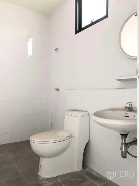 Warehouse for rent in Bang Phli, Samut Prakan - Clean white-tiled bathroom with toilet, sink and small window.