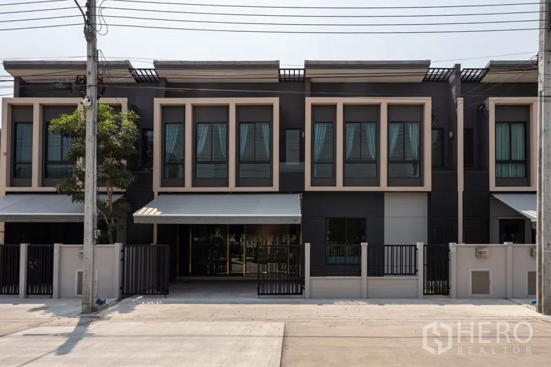 Townhouse for rent in Bang Phli, Samut Prakan - Modern two-storey townhouse facade with large windows, gated frontage and a shaded driveway.