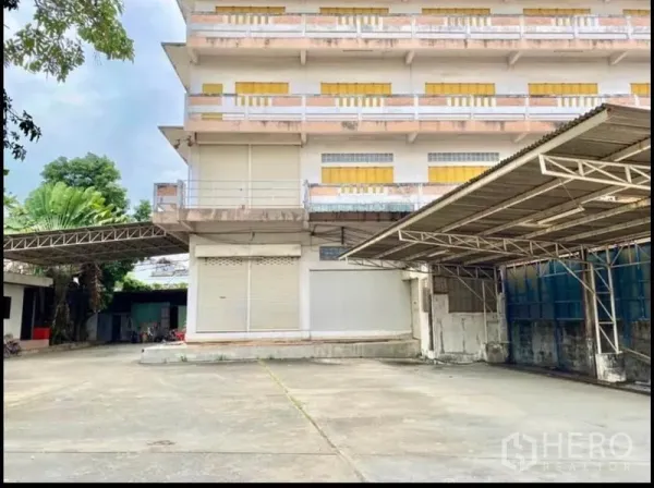 Factory for rent in Chom Thong, Bangkok - Front elevation of the factory with a wide concrete yard and metal canopies for loading.
