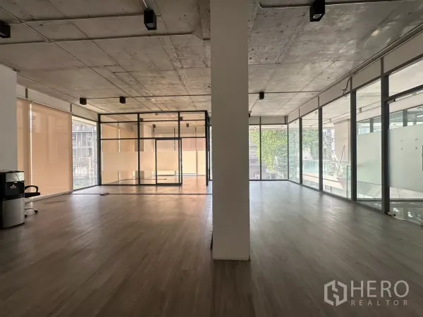 Retail Space for rent - Wide view of the empty corner unit featuring roller blinds, a central column, track lighting, and full-height glazing.