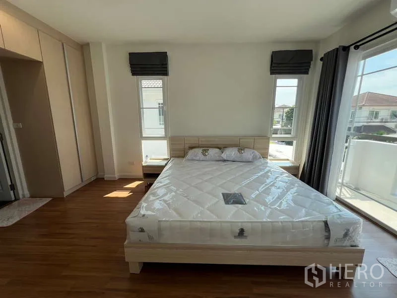 Detached House for rent in Bang Kapi, Bangkok - Master bedroom with large windows, balcony doors and a light wood bed frame.