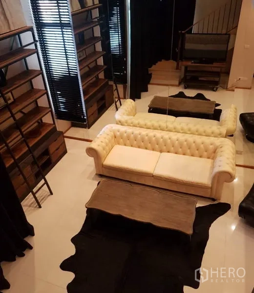 Condominium for rent or sale in Khlong Toei, Bangkok - View from mezzanine over the living area with sofa, shelving and coffee table.