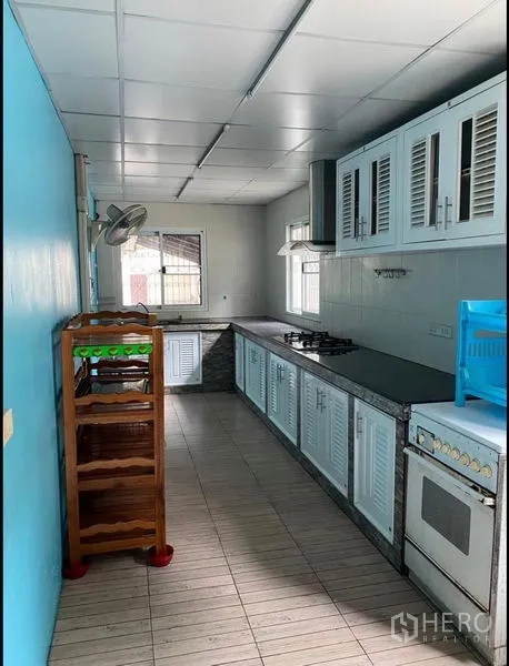 Home Office for rent in Suan Luang, Bangkok - Long galley kitchen with white cabinets, gas hob and windows for ventilation.