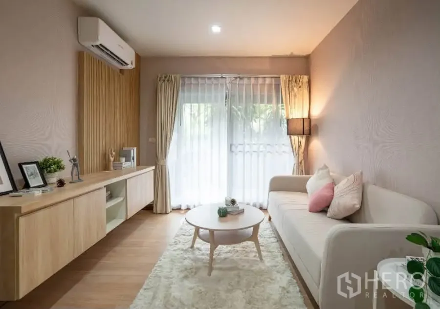 Condominium for rent in Khlong Toei, Bangkok - Cozy lounge with rug, round coffee table and wood accent wall facing the balcony doors.