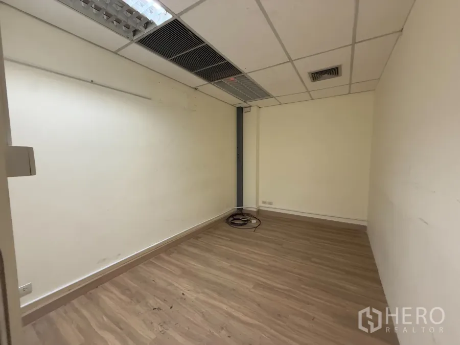 Office Space for rent in Chatuchak, Bangkok - Compact office room with wood-look vinyl flooring, white walls, and a suspended ceiling with air-conditioning vents.