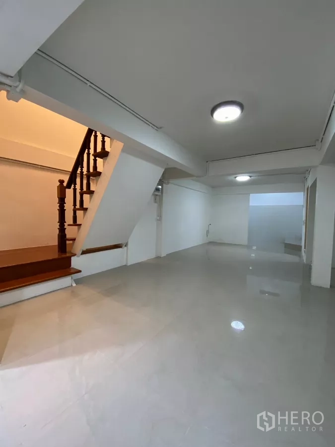 独立式住宅 出租在Bang Na, Bangkok - 木楼梯与开放客厅相邻，墙面素雅，灯光柔和。