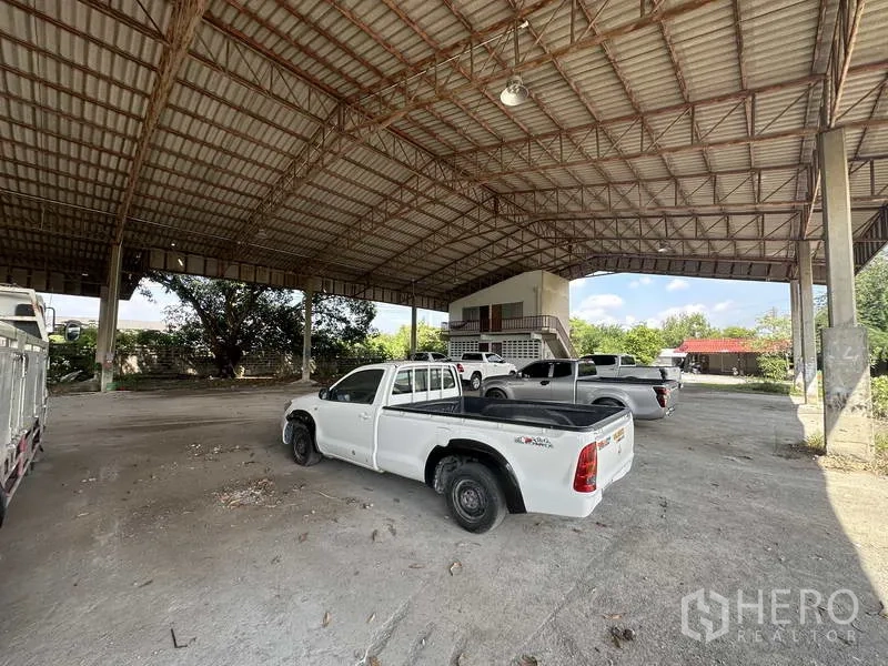 Factory for rent in Phra Nakhon Si Ayutthaya - High-clearance steel-roof warehouse bay with parked pickups and a small office building.