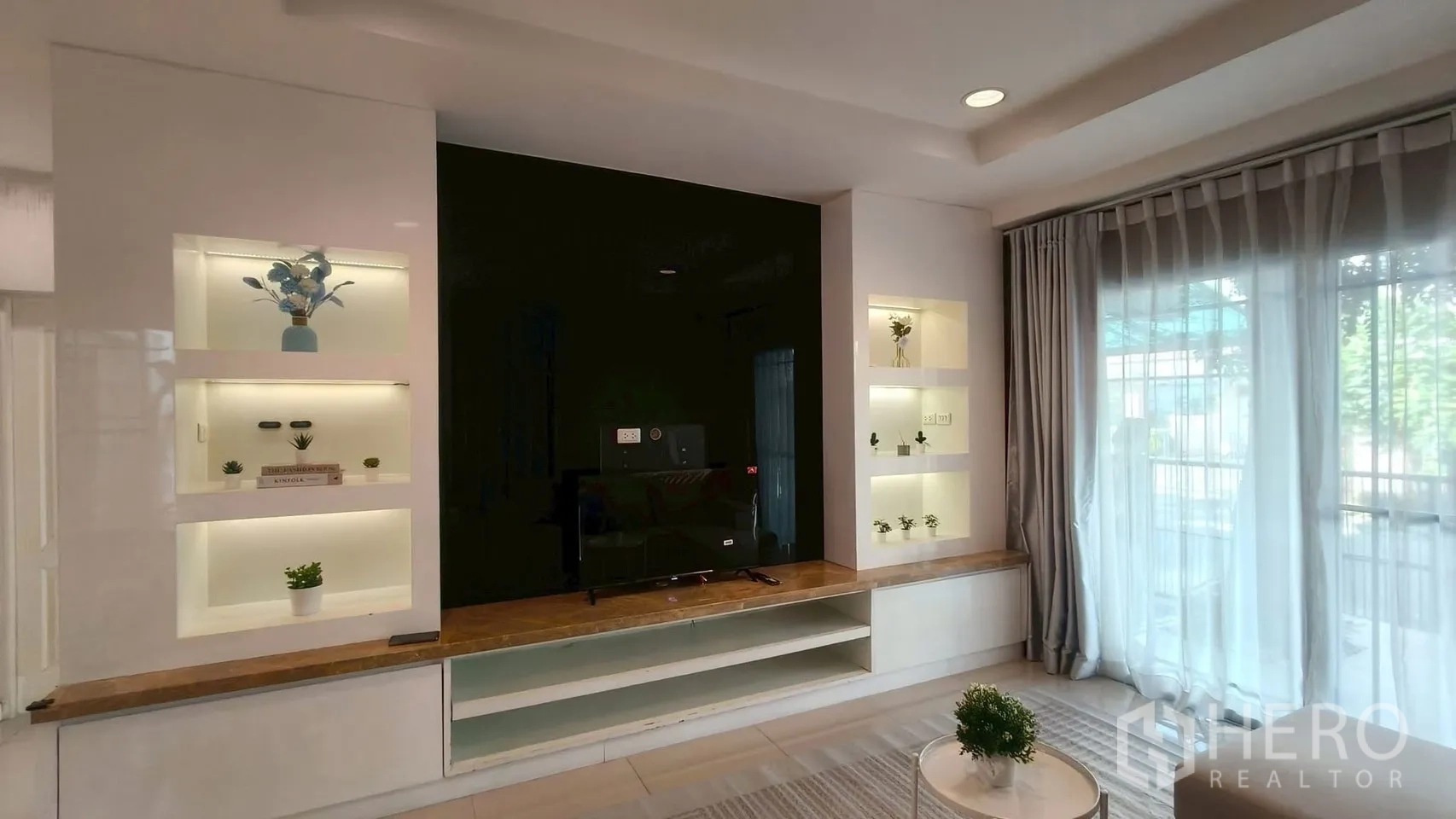 Detached House for rent or sale in Mueang Samut Prakan, Samut Prakan - Living room feature wall with illuminated display shelves, TV unit and sliding glass doors with sheers.