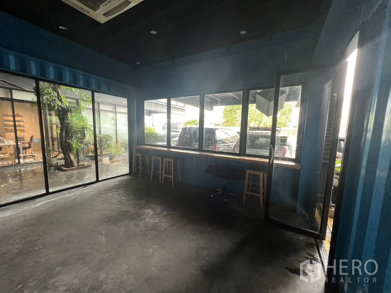 Retail Space for rent - Corner with floor-to-ceiling windows, window bar and stools facing a courtyard with greenery.