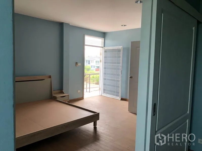 Detached House for sale in Bang Khen, Bangkok - Spacious bedroom with bed frame, sliding door, wood-look flooring and access to a small balcony.