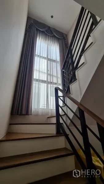 Detached House for sale in Samut Prakan - Staircase with metal balustrade and a tall window bringing natural light.