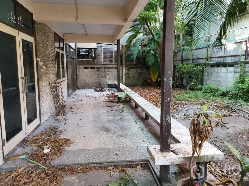 Home Office for rent in Khlong Toei, Bangkok - Covered terrace with long bench, glass doors and overgrown garden.