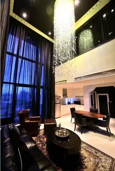 Condominium for rent or sale in Khlong Toei, Bangkok - Open-plan living and dining area with dramatic chandelier, high ceiling and kitchenette in view.