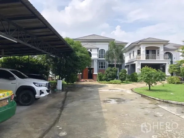 Detached House for sale in Lam Luk Ka, Pathum Thani - Driveway leading to two large two-storey houses and a covered carport.