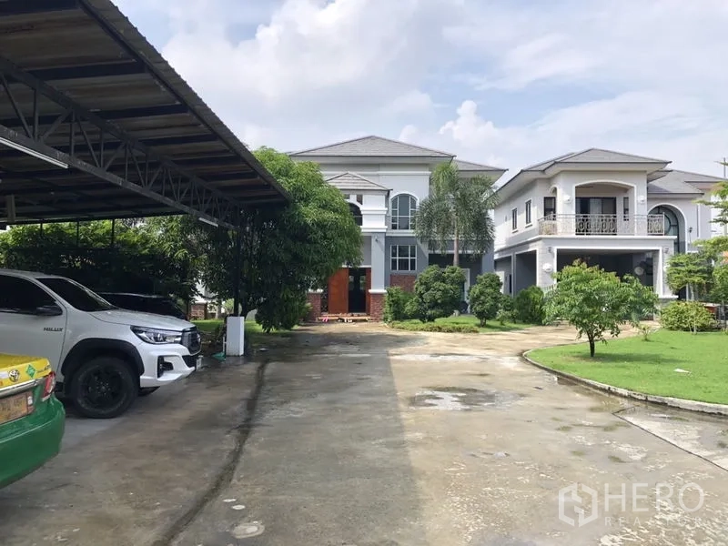 Detached House for sale in Lam Luk Ka, Pathum Thani - Driveway leading to two large two-storey houses and a covered carport.