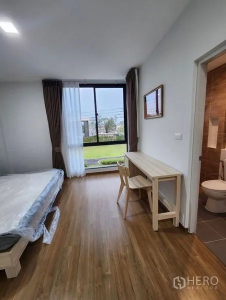 联排别墅 出租在Bang Phli, Samut Prakan - 卧室带大窗面向花园，书桌与套内卫浴连接。