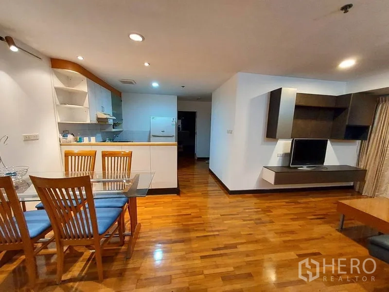 Condominium for rent or sale in Khlong Toei, Bangkok - Spacious open-plan area showing kitchen breakfast bar and mounted TV unit on wooden floors.