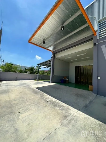 Factory for rent or sale in Lam Luk Ka, Pathum Thani - Covered loading canopy and driveway beside the factory facade ready for truck access.