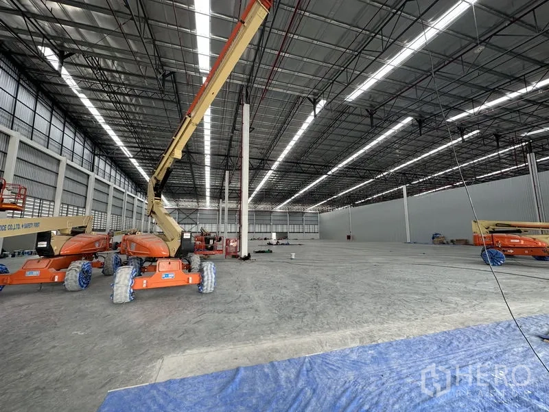 Factory for rent in Khlong Luang, Pathum Thani - Vast high-clearance warehouse with boom lifts and continuous LED strip lighting.