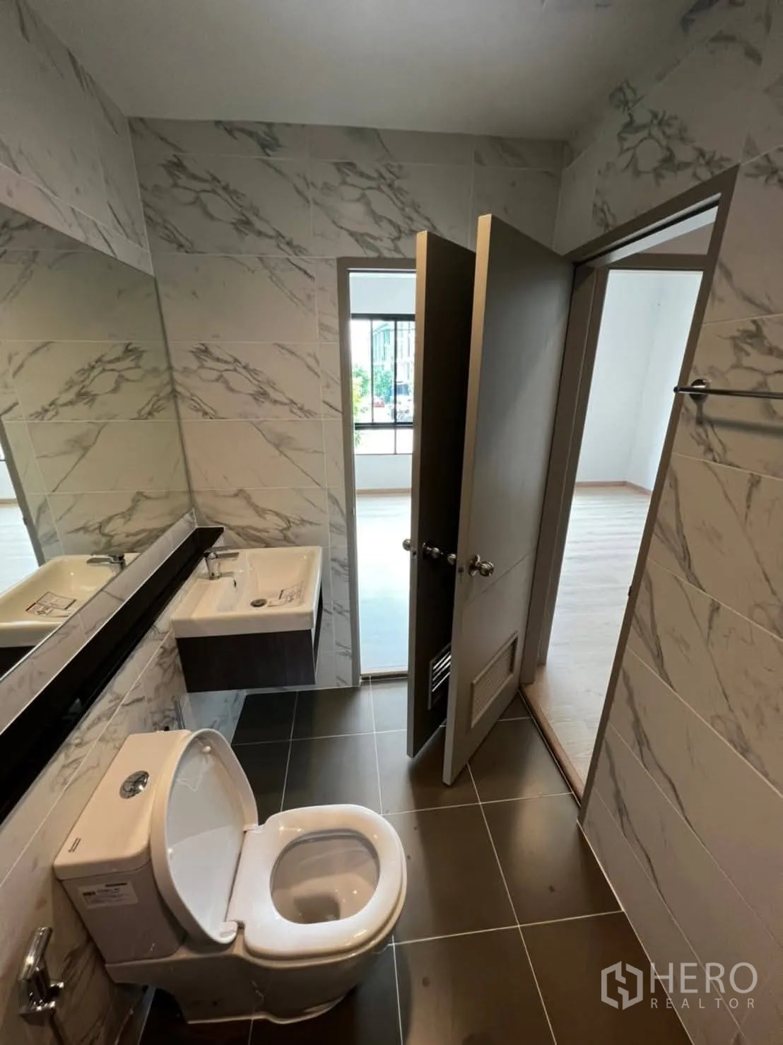 Townhouse for rent in Bang Khen, Bangkok - Sleek bathroom featuring a long mirror, marble-effect walls, and dark floor tiles.