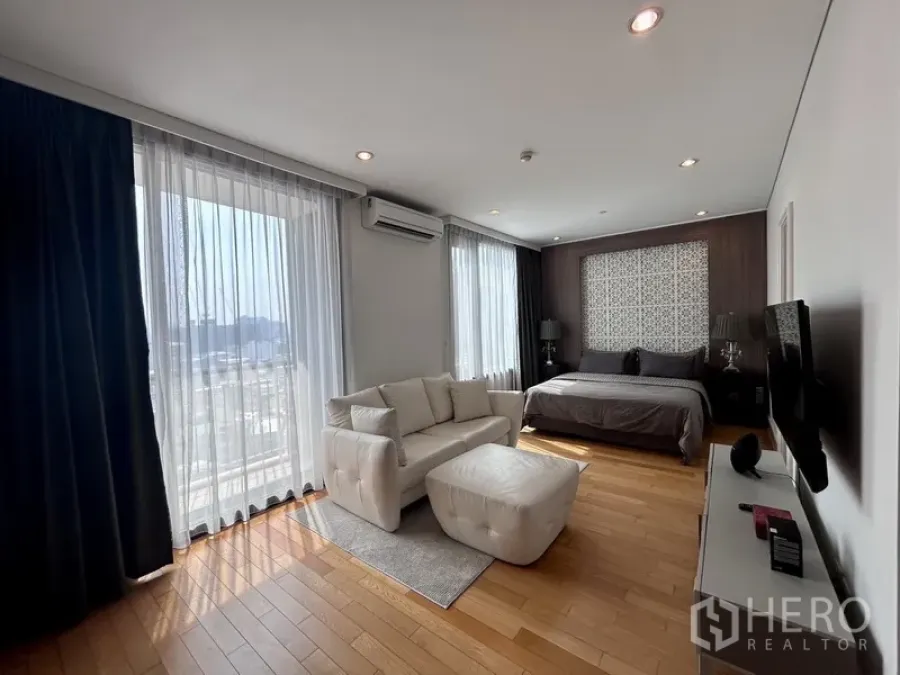 Condominium for rent or sale in Khlong Toei, Bangkok - Bright master bedroom with sofa seating, hardwood floors and full-height windows with city view.