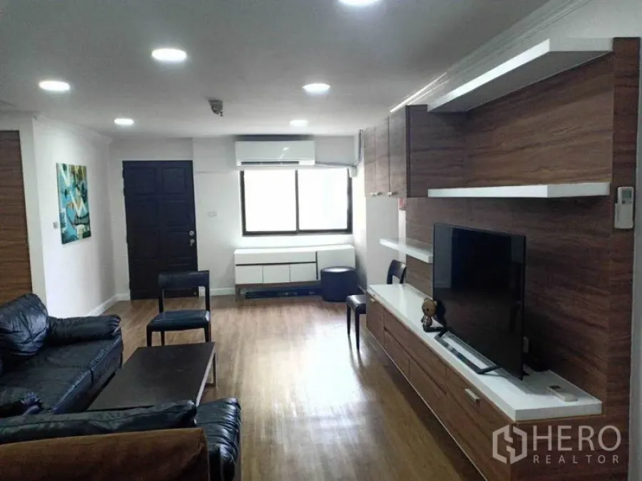 Condominium for rent in Watthana, Bangkok - Bright living room with wood floors, built-in TV wall and leather sofa in Phrom Phong condo
