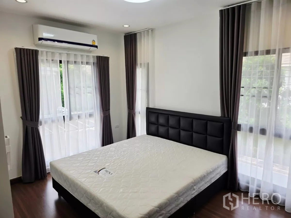 Detached House for rent in Prawet, Bangkok - Bedroom with large bed, corner windows, sheer drapes and wall-mounted air conditioner.