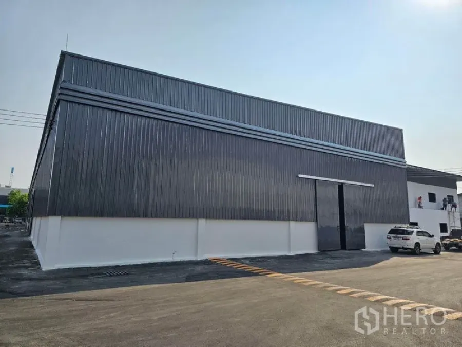 Warehouse for rent in Khlong Toei, Bangkok - Front facade of warehouse unit with tall sliding loading door and adjacent car parking.