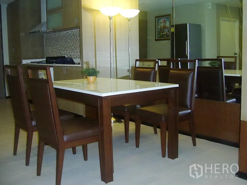 Condominium for rent in Khlong Toei, Bangkok - Dining area with six-seat wooden table beside modern kitchen, mirror wall and standing lamp in a Bangkok condo.