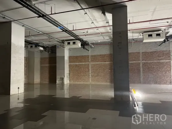 Retail Space for rent - Open-plan shop area featuring brick accent walls, structural columns and ceiling AC units.