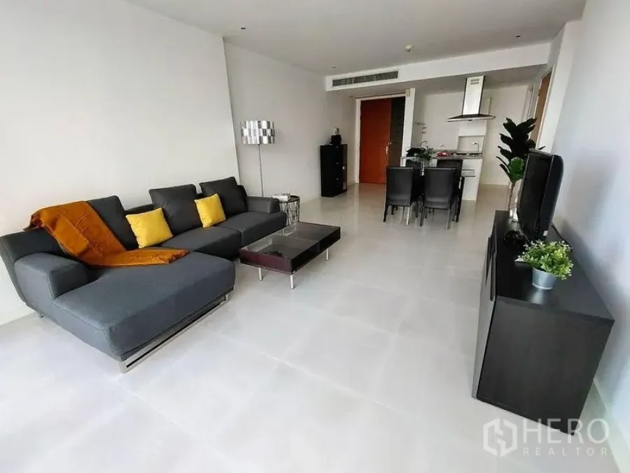 公寓 出租在Watthana, Bangkok - 宽敞客厅，转角沙发与电视柜，推拉大玻璃门通向城市景观。